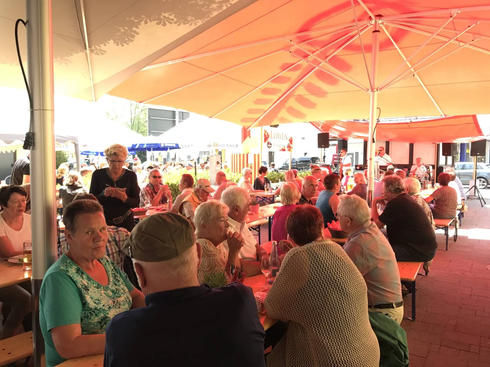Gäste unter roten Sonnenschirmen im Biergarten