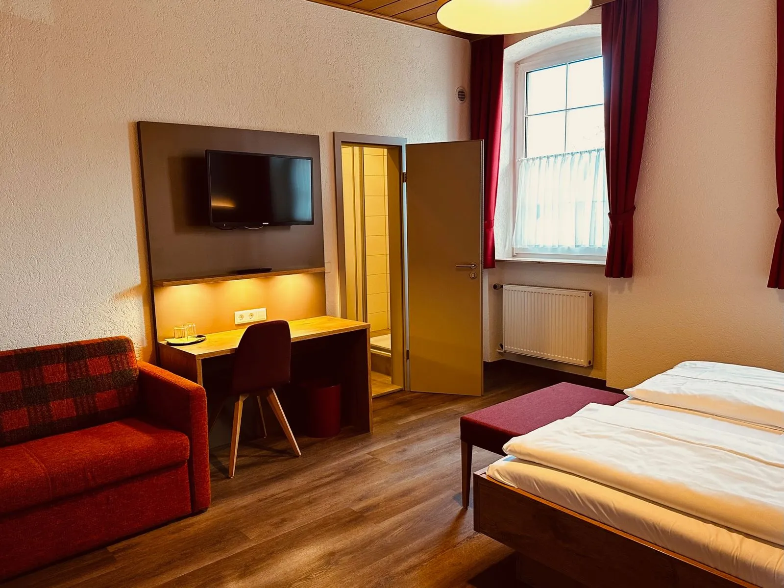 Zimmer mit roter Sitzecke, Schreibtisch und Flachbild-TV